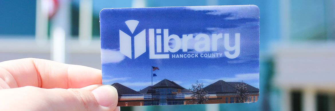 Someone holding a library card in front of the library building