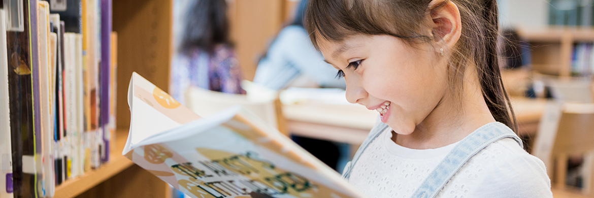 Young girl smiling as she looks into a book in the library
