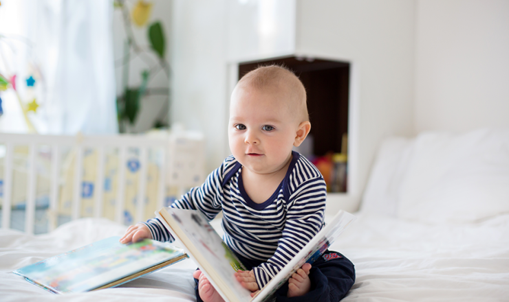 Baby sitting on bed with open book
