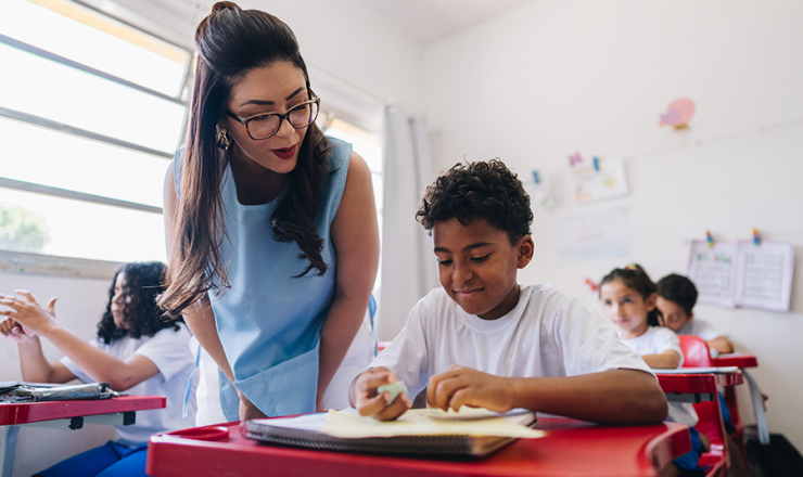 Female teacher leaning over a desk to help a boy with work
