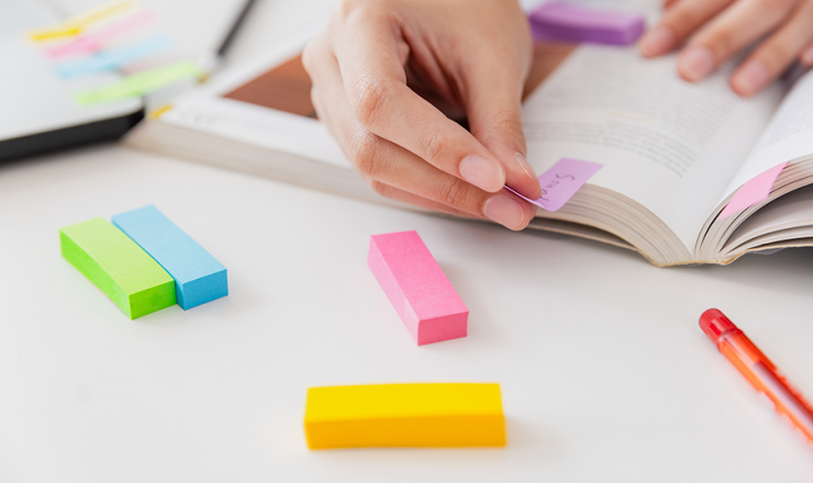 Person bookmarking passages in a textbook with small post-it tabs