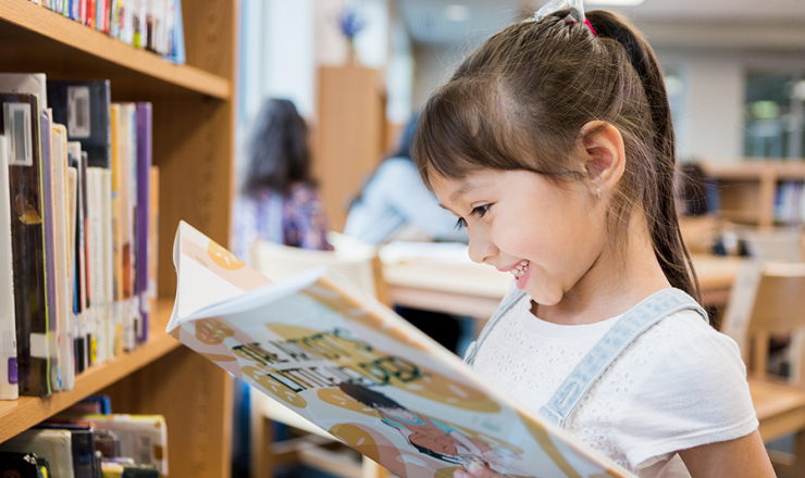 Young girl smiling as she looks into a book in the library